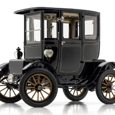 Seitenansicht eines restaurierten 1912 Baker Electric Model V Special Extension Coupe mit schwarz-goldenen Rädern und klassischer Aluminiumkarosserie.