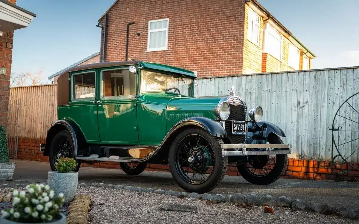 Grüner Ford Model A Baujahr 1928 mit schwarzem Dach und Speichenrädern steht vor einem Haus in der Einfahrt.