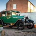 Grüner Ford Model A Baujahr 1928 mit schwarzem Dach und Speichenrädern steht vor einem Haus in der Einfahrt.