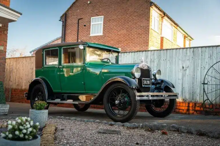 Grüner Ford Model A Baujahr 1928 mit schwarzem Dach und Speichenrädern steht vor einem Haus in der Einfahrt.