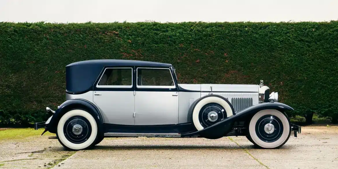 Seitenansicht eines 1930 Bentley Speed Six mit zweifarbiger Schutte-Karosserie vor einer grünen Hecke.
