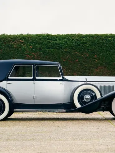 Seitenansicht eines 1930 Bentley Speed Six mit zweifarbiger Schutte-Karosserie vor einer grünen Hecke.