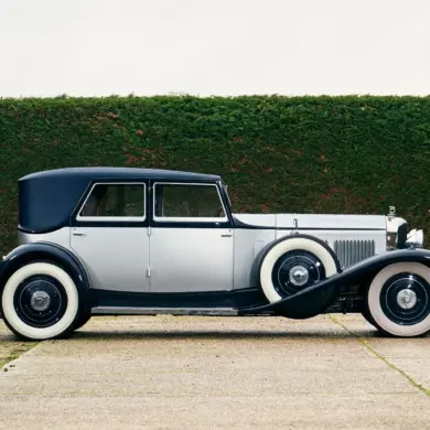 Seitenansicht eines 1930 Bentley Speed Six mit zweifarbiger Schutte-Karosserie vor einer grünen Hecke.