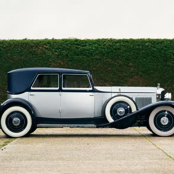 Seitenansicht eines 1930 Bentley Speed Six mit zweifarbiger Schutte-Karosserie vor einer grünen Hecke.