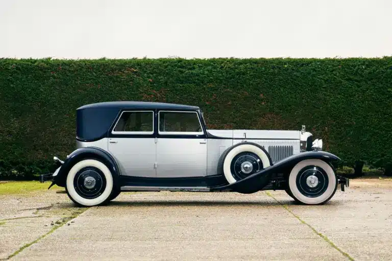 Seitenansicht eines 1930 Bentley Speed Six mit zweifarbiger Schutte-Karosserie vor einer grünen Hecke.