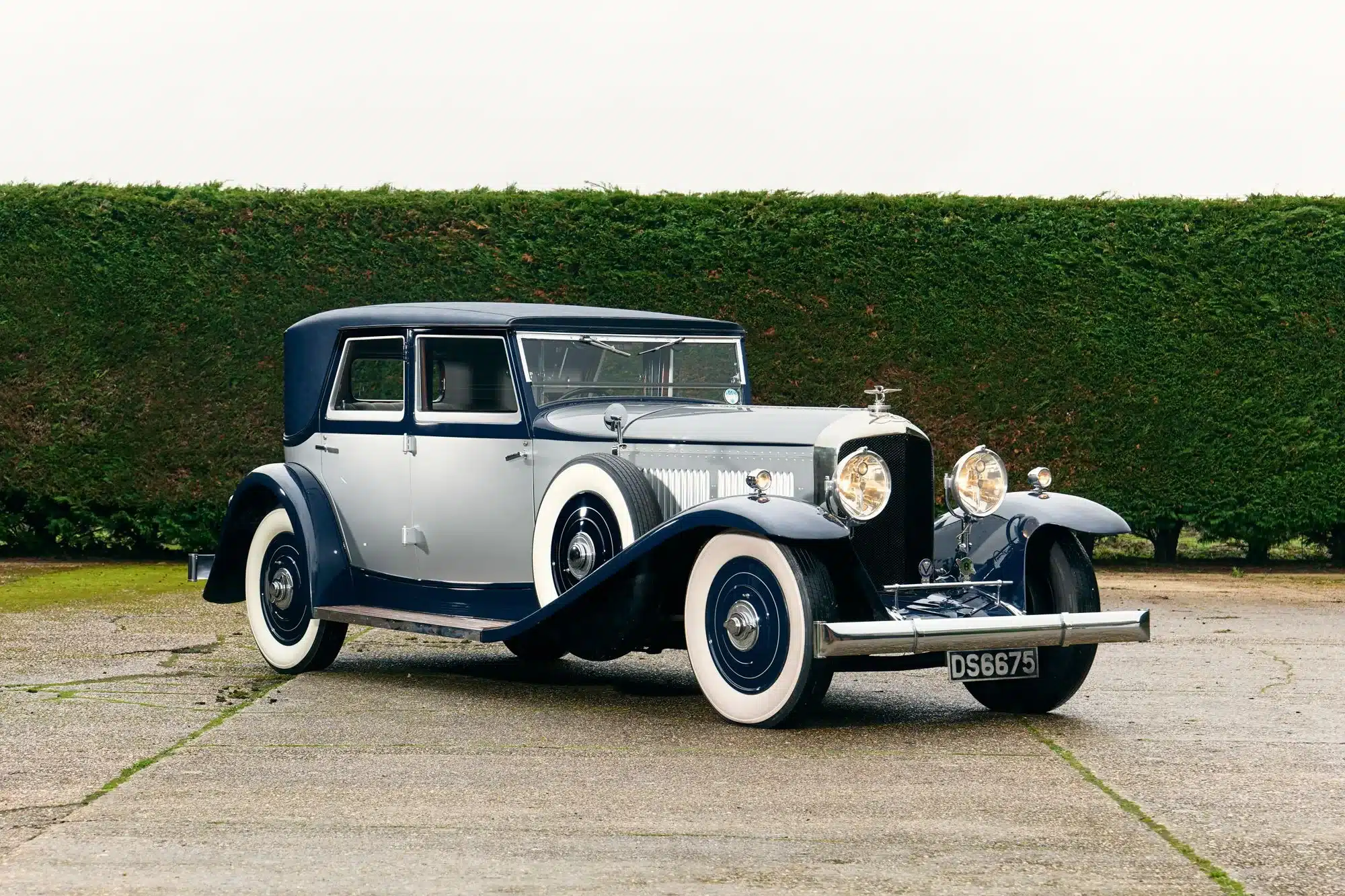 Seitenansicht eines restaurierten 1930 Bentley Speed Six mit Schutte-Karosserie, zweifarbig lackiert, vor Hecken stehend.