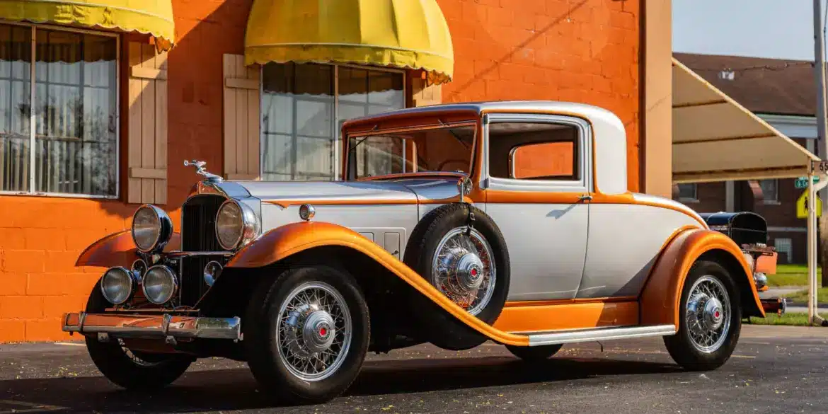 Front- und Seitenansicht eines silber-orangefarbenen Packard Model 902 Eight Coupé von 1932, geparkt vor einem Gebäude mit gelben Markisen.