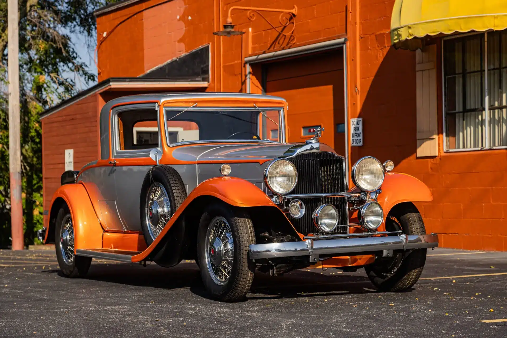 Frontalansicht eines Packard Model 902 Eight Coupé von 1932 in orange-grauer Lackierung, geparkt vor einem historischen Gebäude.