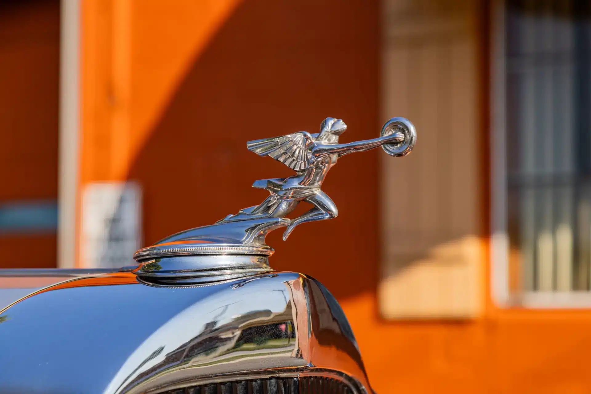 Nahaufnahme der klassischen geflügelten Packard-Kühlerfigur auf einem glänzenden Kotflügel des Coupés, historischer Hintergrund unscharf.