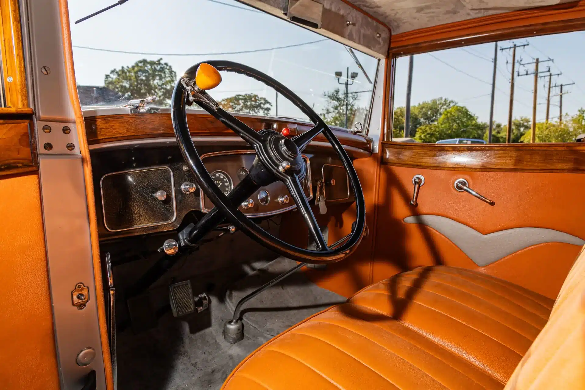Innenraum mit Lenkrad und Armaturenbrett eines Packard 902 Eight Coupé von 1932, orangefarbene Ledersitze, Holzzierleisten und originale Bedienelemente.