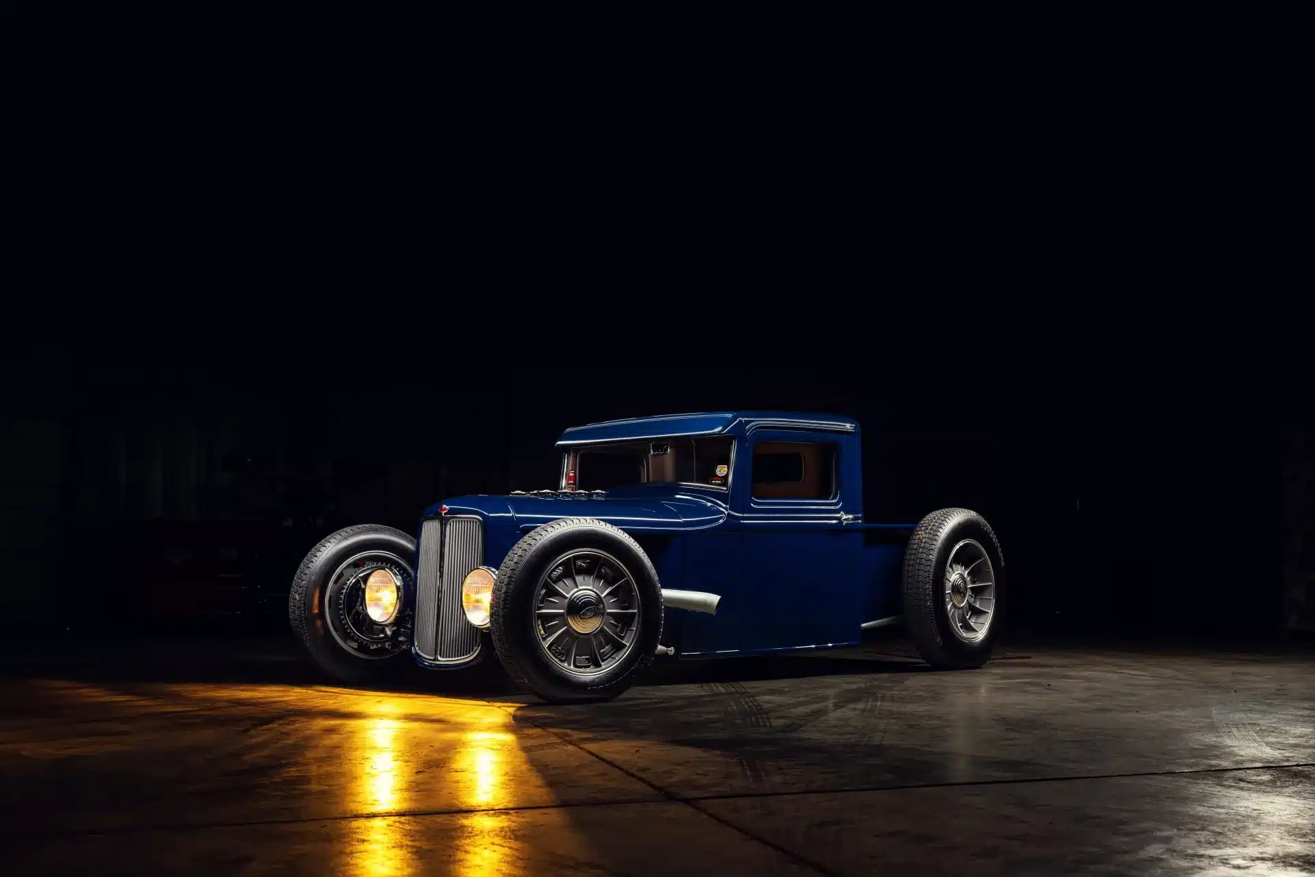 Blauer 1934 Ford Model A Hot Rod Pickup mit modernisierten Details und tiefen Scheinwerfern in einer Halle, seitlich aufgenommen.