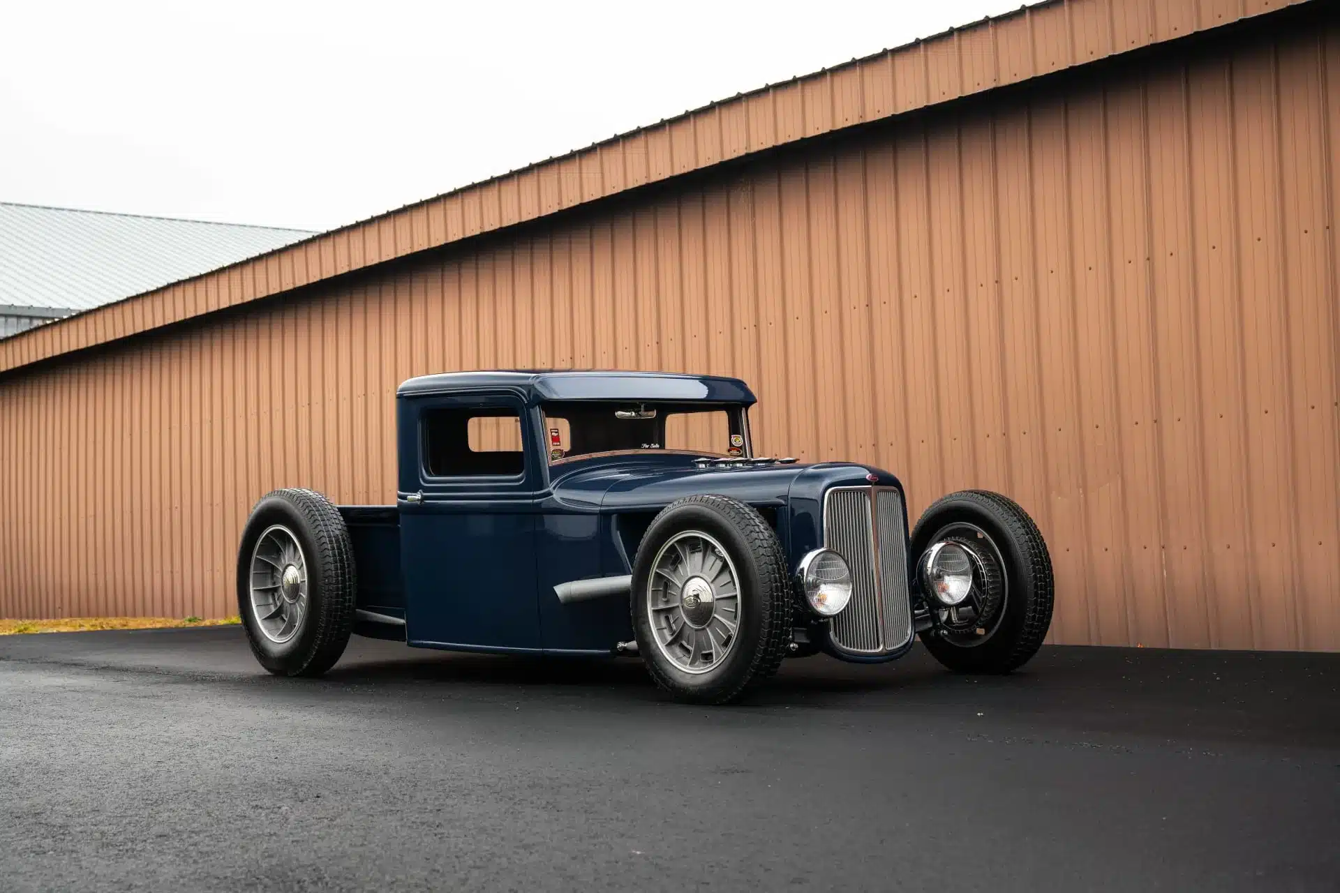 Umgebauter 1934 Ford Model A Hot Rod Pickup in Blau von der Seite vor einer Halle.