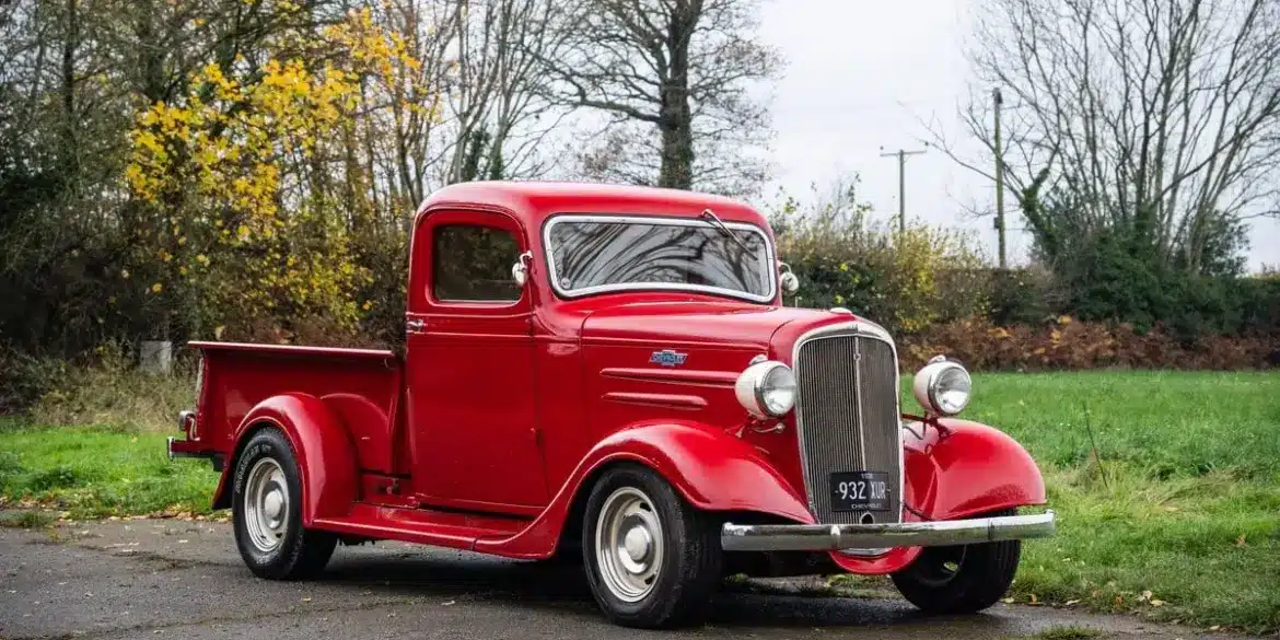 Restaurierter roter 1936 Chevrolet FB Pickup mit Chromakzenten, geparkt im Freien vor Bäumen.