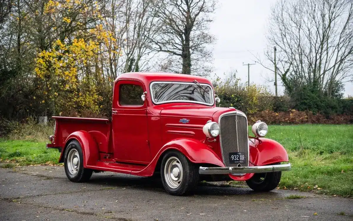 Restaurierter roter 1936 Chevrolet FB Pickup mit Chromakzenten, geparkt im Freien vor Bäumen.