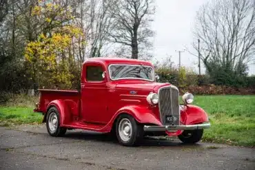 Restaurierter roter 1936 Chevrolet FB Pickup mit Chromakzenten, geparkt im Freien vor Bäumen.
