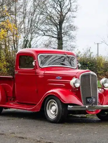 Restaurierter roter 1936 Chevrolet FB Pickup mit Chromakzenten, geparkt im Freien vor Bäumen.