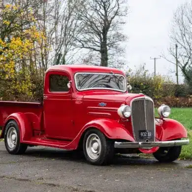 Restaurierter roter 1936 Chevrolet FB Pickup mit Chromakzenten, geparkt im Freien vor Bäumen.