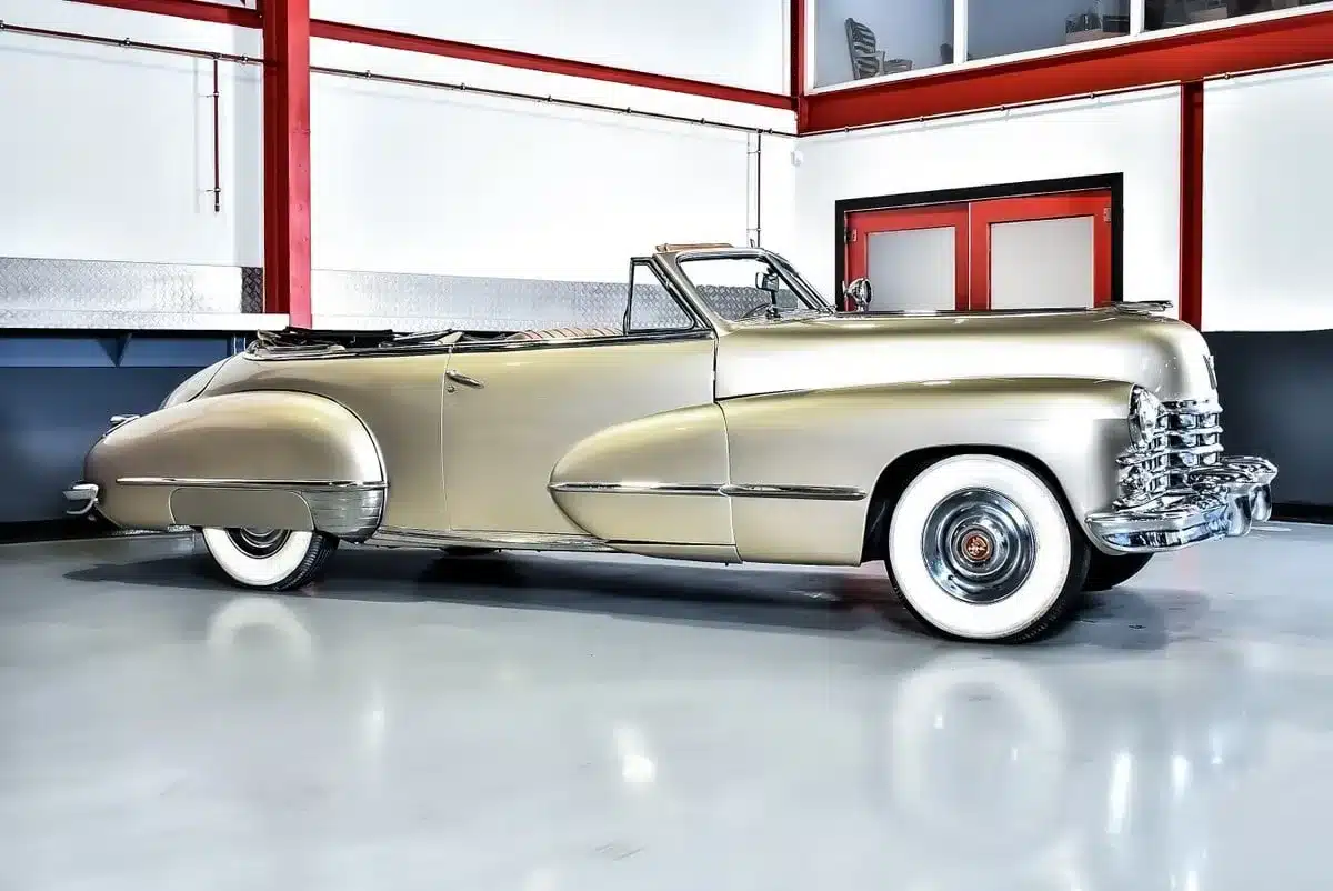 Cadillac Series 62 Cabriolet Baujahr 1947 in metallic Champagnergold, Seitenansicht, restauriert im Innenraum einer modernen Halle.