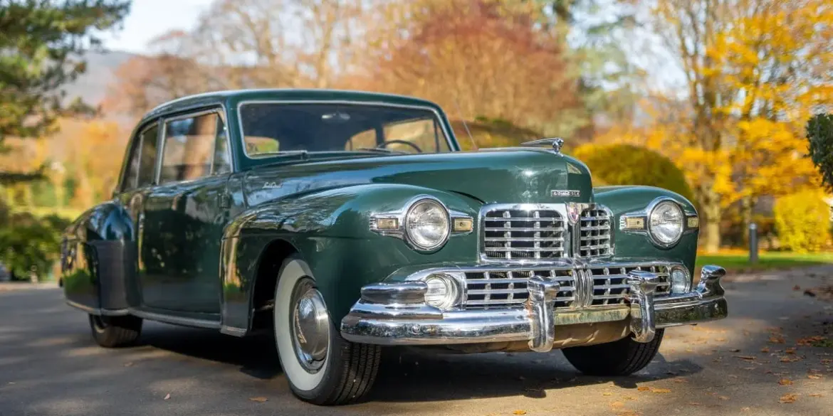 Dunkelgrünes 1948 Lincoln Continental Coupé mit V12-Motor, geparkt auf einer herbstlichen Straße.