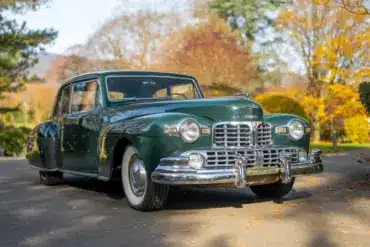 Dunkelgrünes 1948 Lincoln Continental Coupé mit V12-Motor, geparkt auf einer herbstlichen Straße.