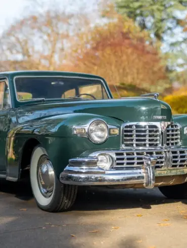 Dunkelgrünes 1948 Lincoln Continental Coupé mit V12-Motor, geparkt auf einer herbstlichen Straße.