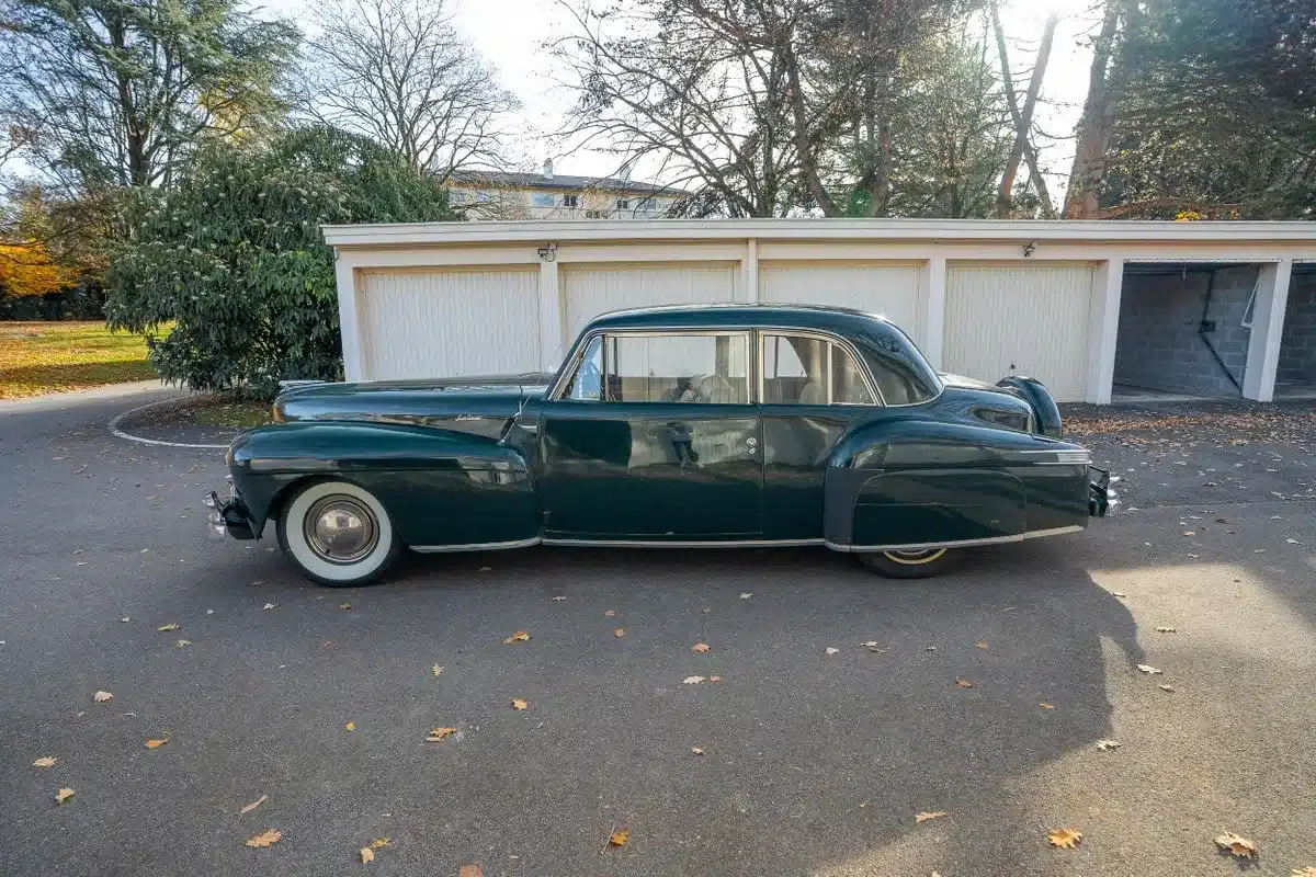 Dunkelgrünes Lincoln Continental Coupé von 1948, geparkt vor Garagen, Seitenansicht.