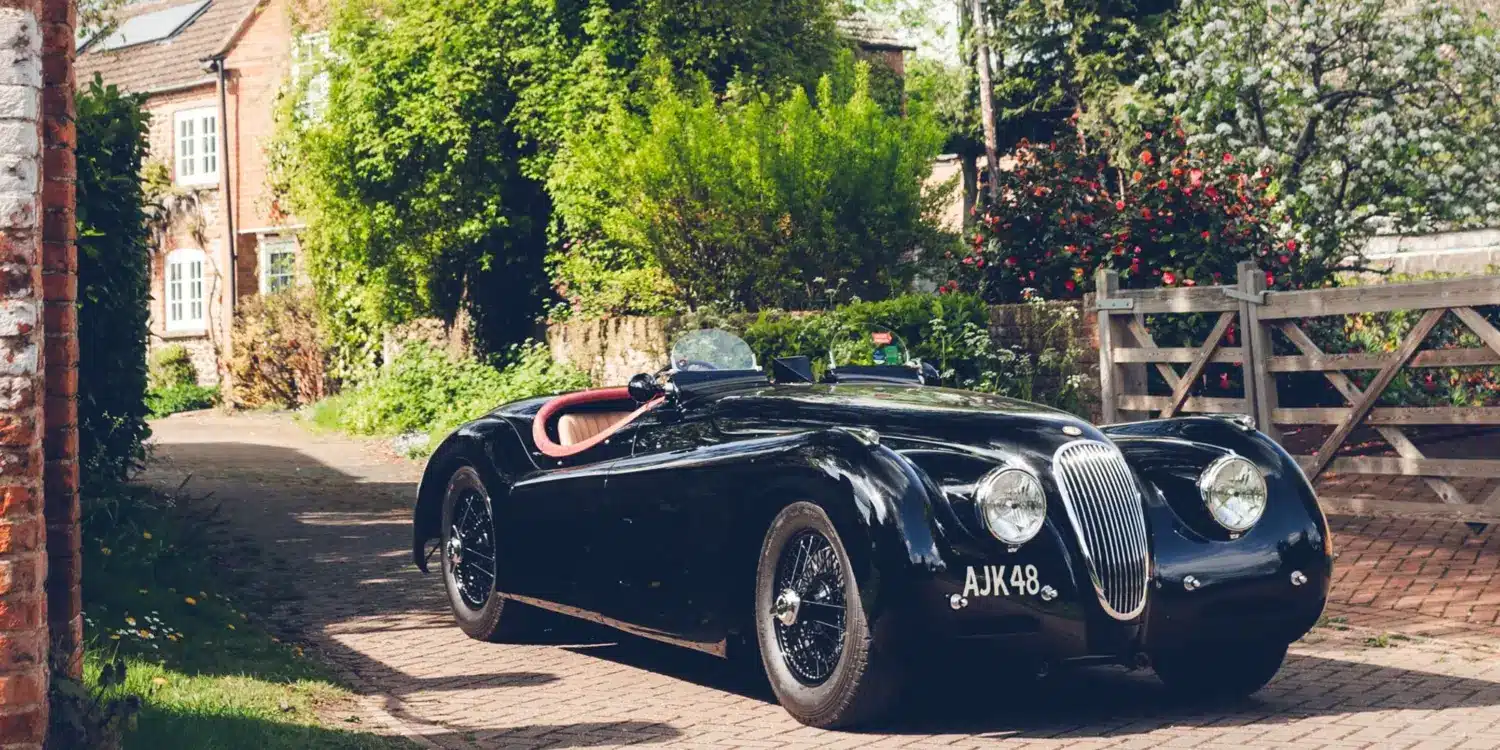 Schwarzer Jaguar XK120 Roadster von 1951 mit rotem und Biscuit-farbenem Interieur vor einem Landhaus