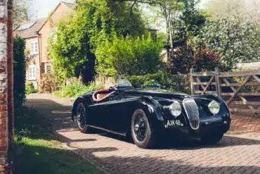 Schwarzer Jaguar XK120 Roadster von 1951 mit rotem und Biscuit-farbenem Interieur vor einem Landhaus