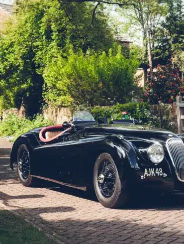 Schwarzer Jaguar XK120 Roadster von 1951 mit rotem und Biscuit-farbenem Interieur vor einem Landhaus