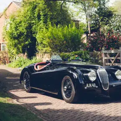 Schwarzer Jaguar XK120 Roadster von 1951 mit rotem und Biscuit-farbenem Interieur vor einem Landhaus