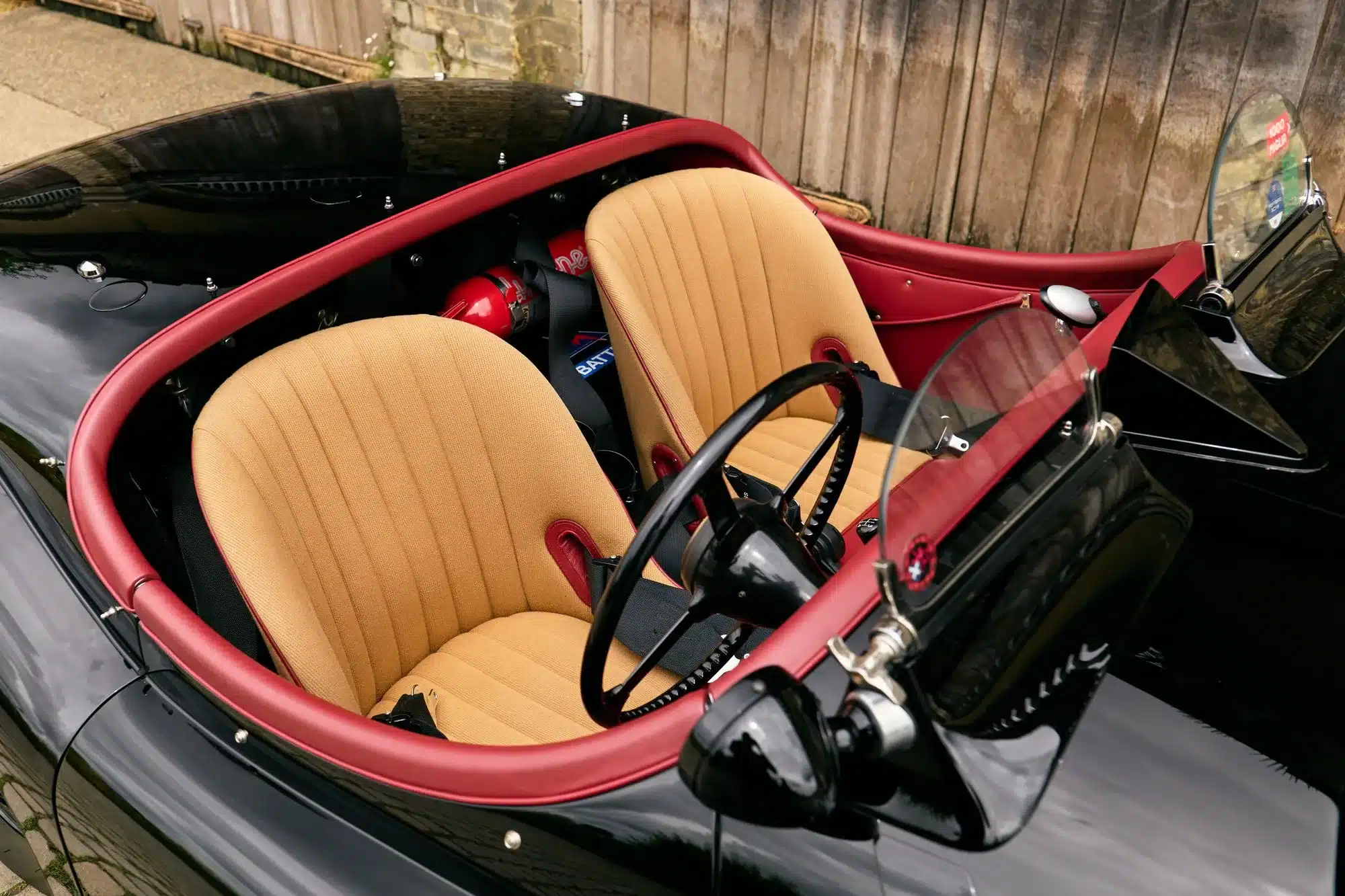 Innenraum eines schwarzen Jaguar XK120 Roadster von 1951 mit Biscuit-farbenen Competition-Sitzen und roten Akzenten.