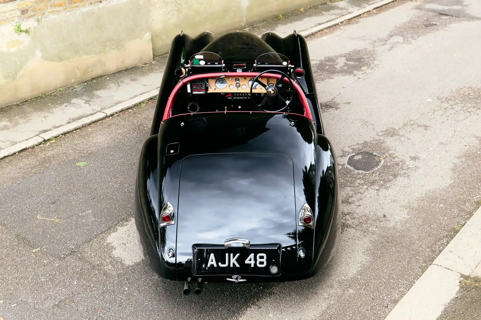 Schwarz lackierter Jaguar XK120 Roadster von 1951, Rückansicht, mit rotem Überrollbügel und sportlichem Cockpit.