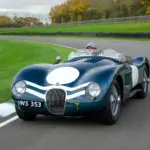 Jaguar C-Type XKC 006 in Dunkelgrün mit weißer Startnummer auf Rennstrecke, Frontansicht, Fahrer mit Schiebermütze