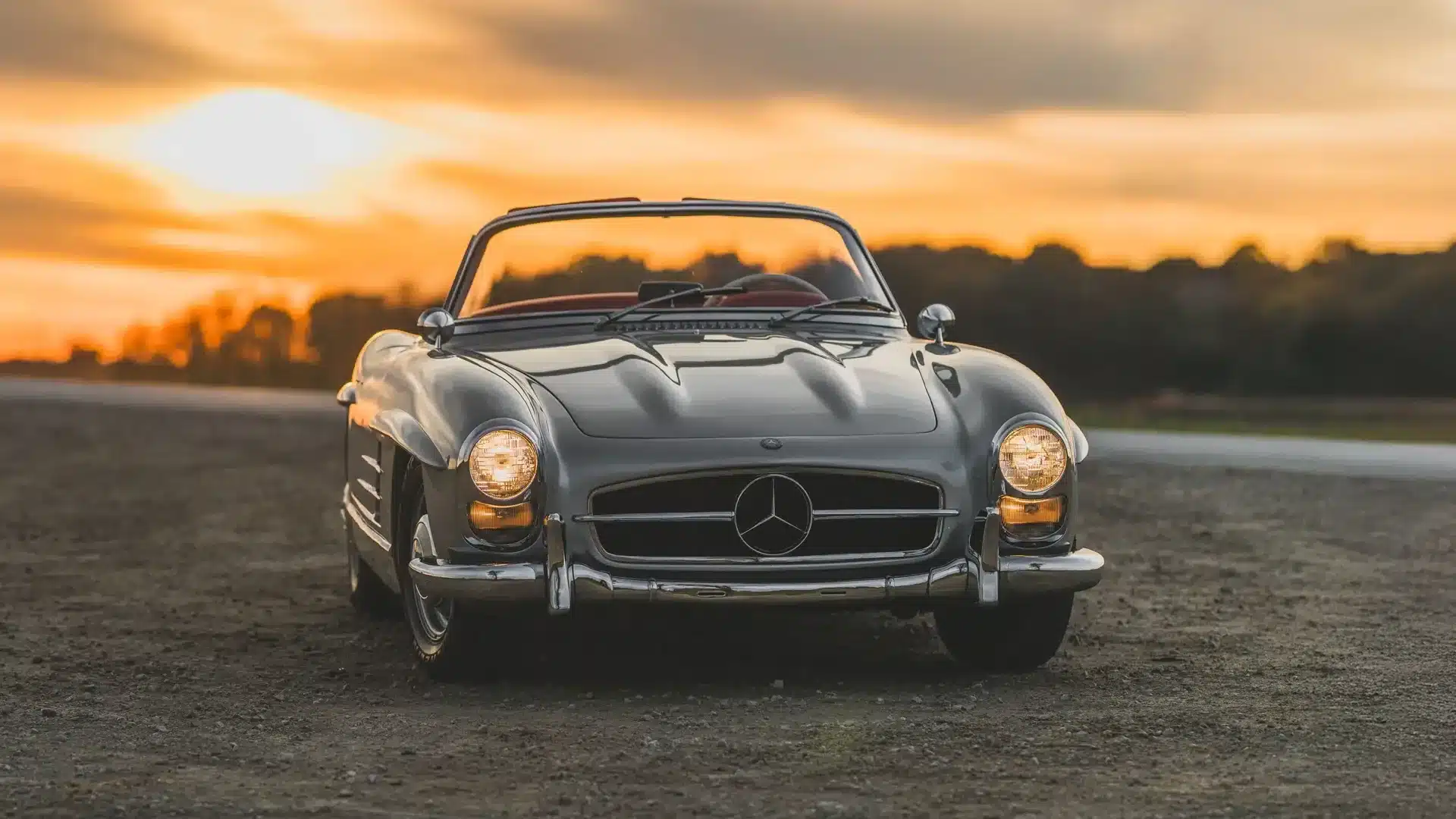 Mercedes-Benz 300 SL Roadster, Baujahr 1957, silberfarben mit rotem Interieur, frontal fotografiert bei Sonnenuntergang.