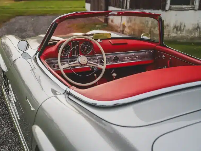 Der Innenraum eines silbernen Mercedes-Benz 300 SL Roadster von 1957 mit rotem Leder und offenem Dach, aufgenommen von hinten.