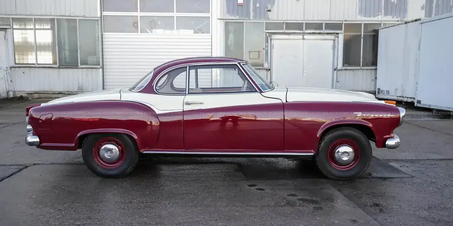 Borgward Isabella Coupé von 1961 in bordeaux-weißer Zweifarblackierung, Seitenansicht vor Werkshalle.