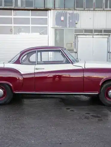 Borgward Isabella Coupé von 1961 in bordeaux-weißer Zweifarblackierung, Seitenansicht vor Werkshalle.