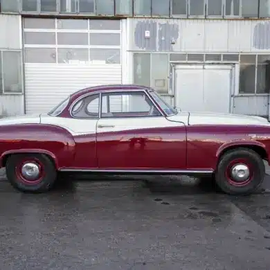 Borgward Isabella Coupé von 1961 in bordeaux-weißer Zweifarblackierung, Seitenansicht vor Werkshalle.