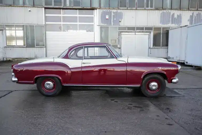 Borgward Isabella Coupé von 1961 in bordeaux-weißer Zweifarblackierung, Seitenansicht vor Werkshalle.