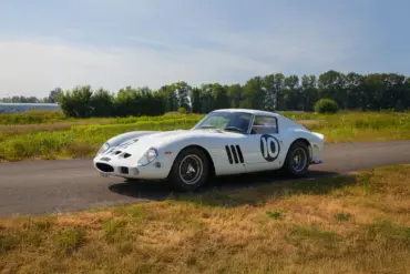 Weißer Ferrari 250 GTO von 1962 mit Rennnummer 10 auf einer Landstraße im Grünen.