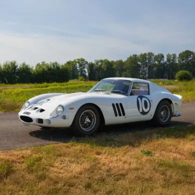 Weißer Ferrari 250 GTO von 1962 mit Rennnummer 10 auf einer Landstraße im Grünen.