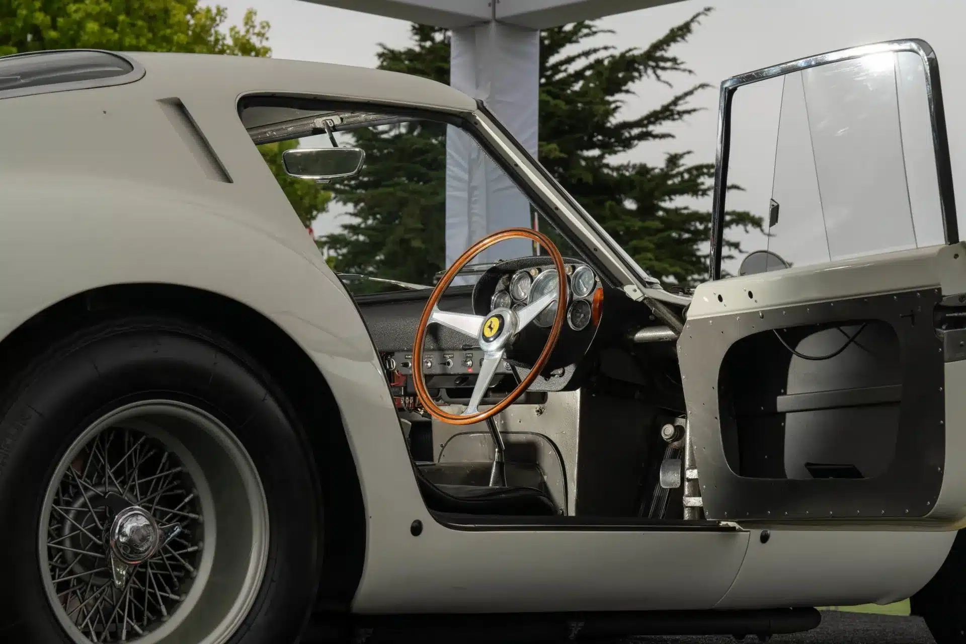 Innenraum und Lenkrad eines Ferrari 250 GTO aus dem Jahr 1962 mit geöffneter Fahrertür, Aluminiumverkleidungen und Holzlenkrad.