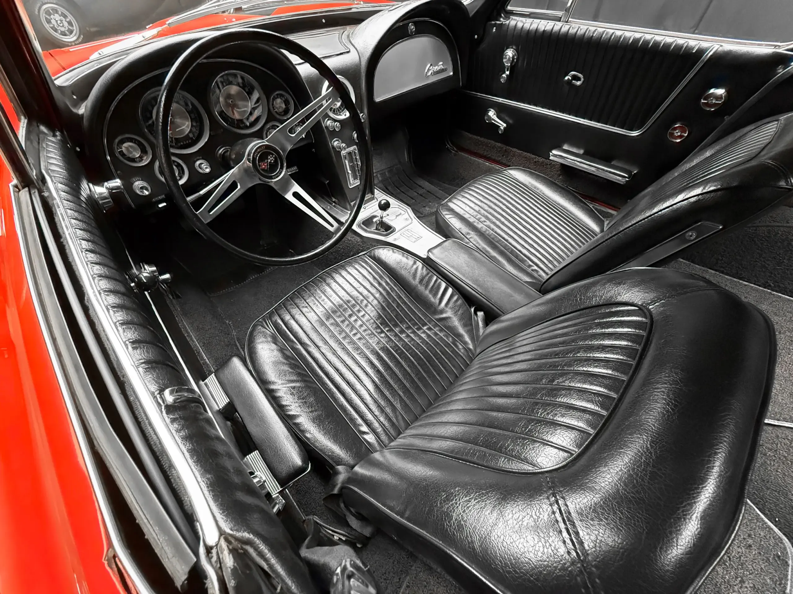 Innenraum einer 1963 Chevrolet Corvette Split-Window mit schwarzem Vinyl, klassischen Armaturen und Lenkrad.