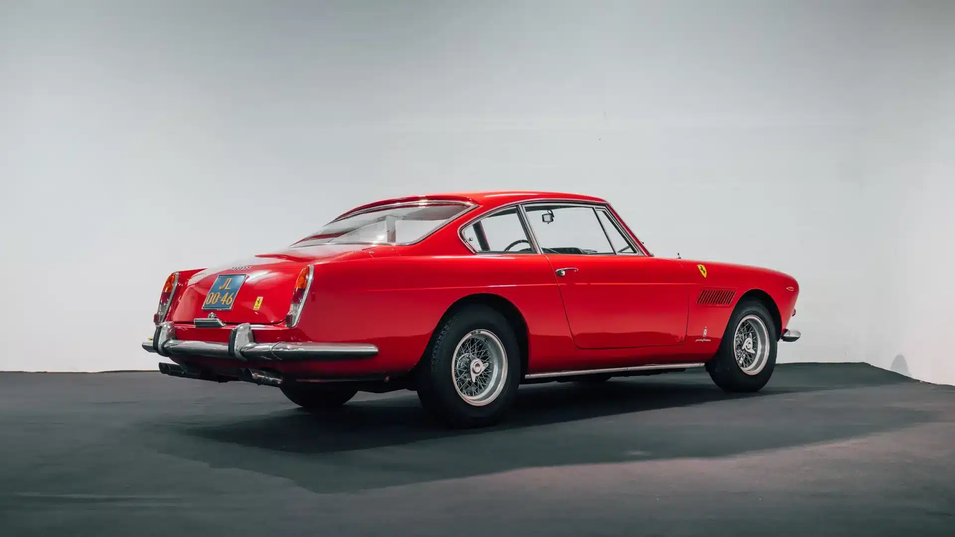 Roter Ferrari 250 GTE 2+2 Series III von 1963, fotografiert schräg von hinten in einer hellen Studioumgebung.