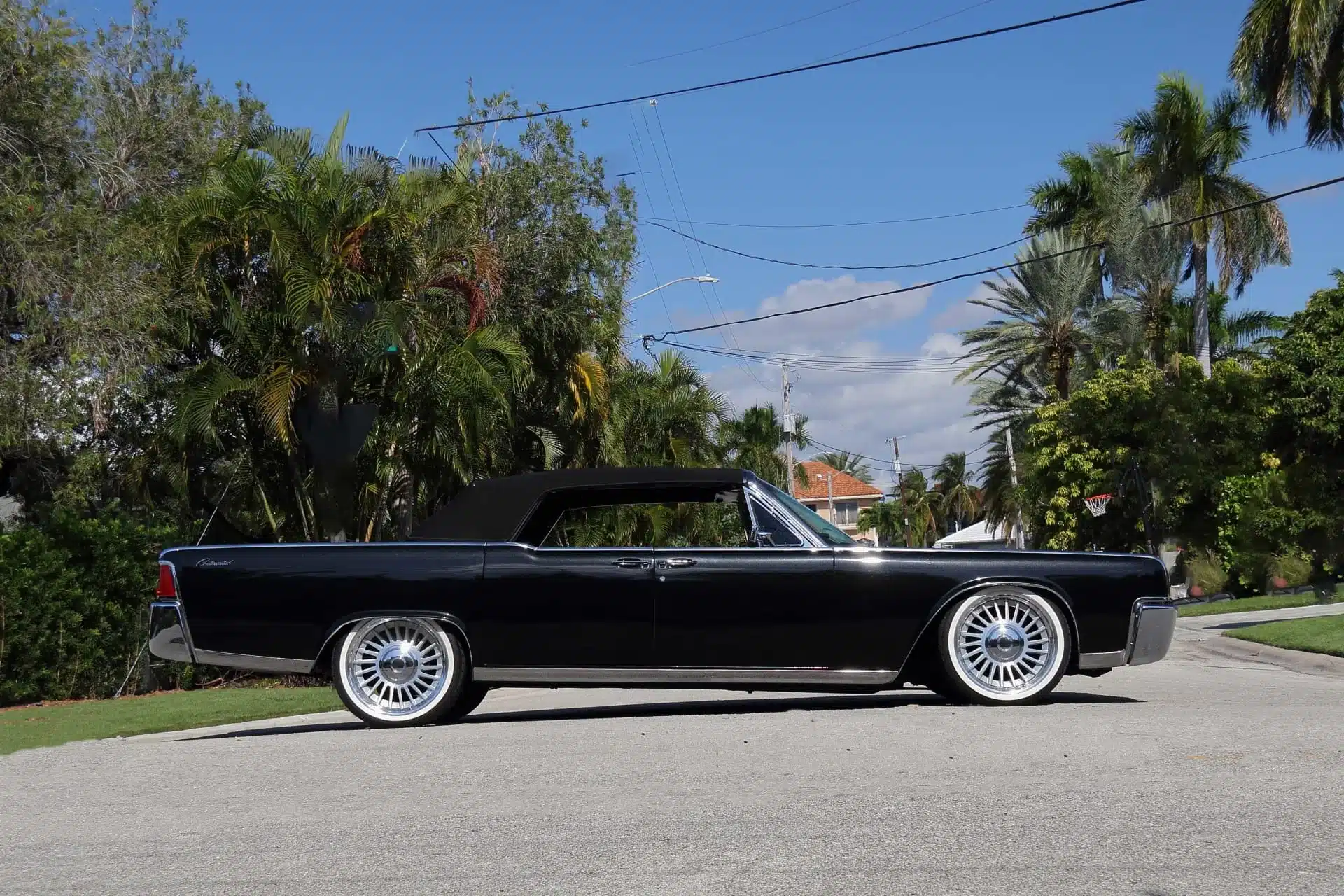 Schwarzes 1964 Lincoln Continental Cabriolet mit geschlossenem Verdeck und custom Felgen, fotografiert bei Tageslicht in einer tropischen Wohngegend.