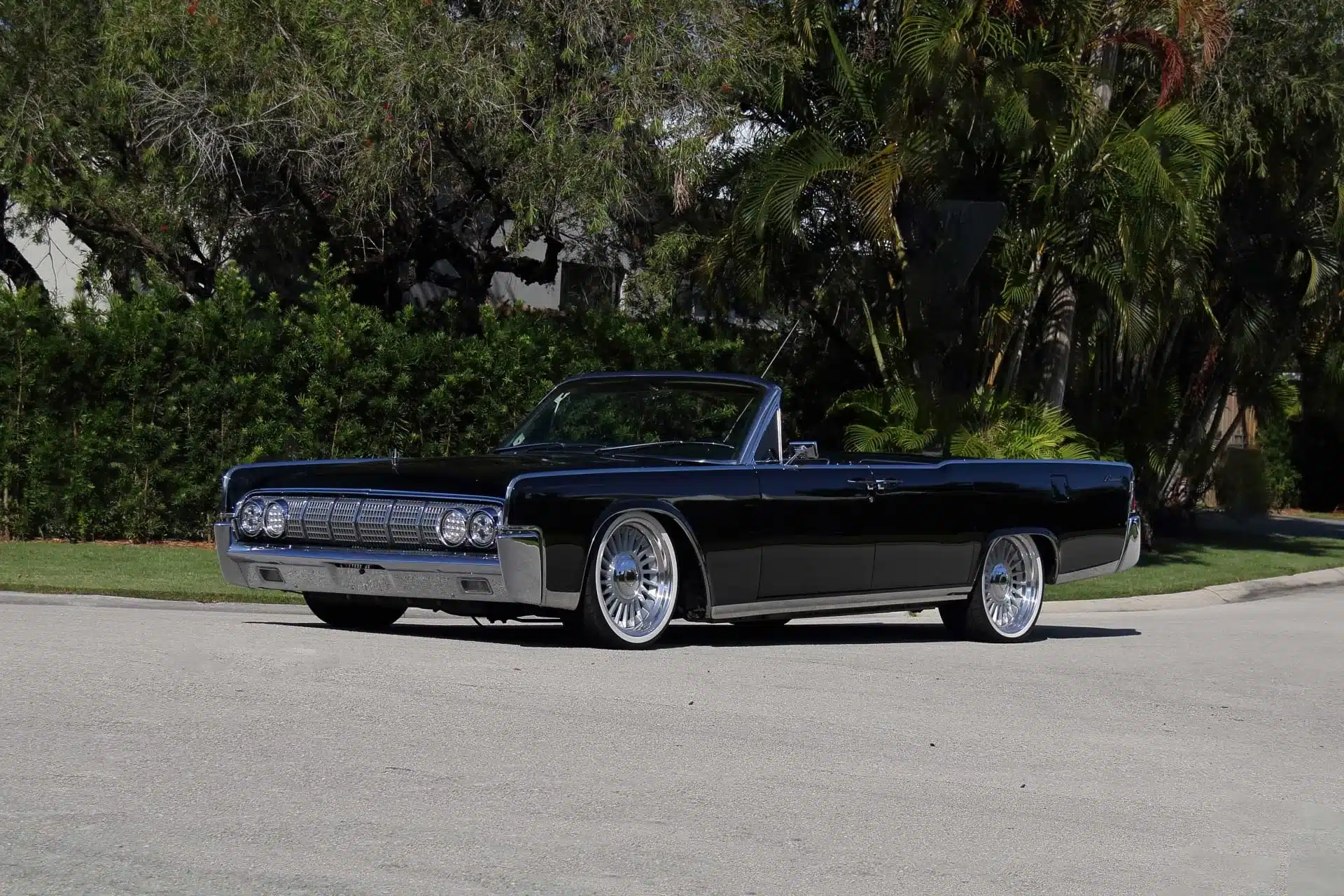 Schwarzes 1964 Lincoln Continental Cabriolet mit offenem Verdeck, modernen Felgen und charakteristischem Design, geparkt im Grünen.