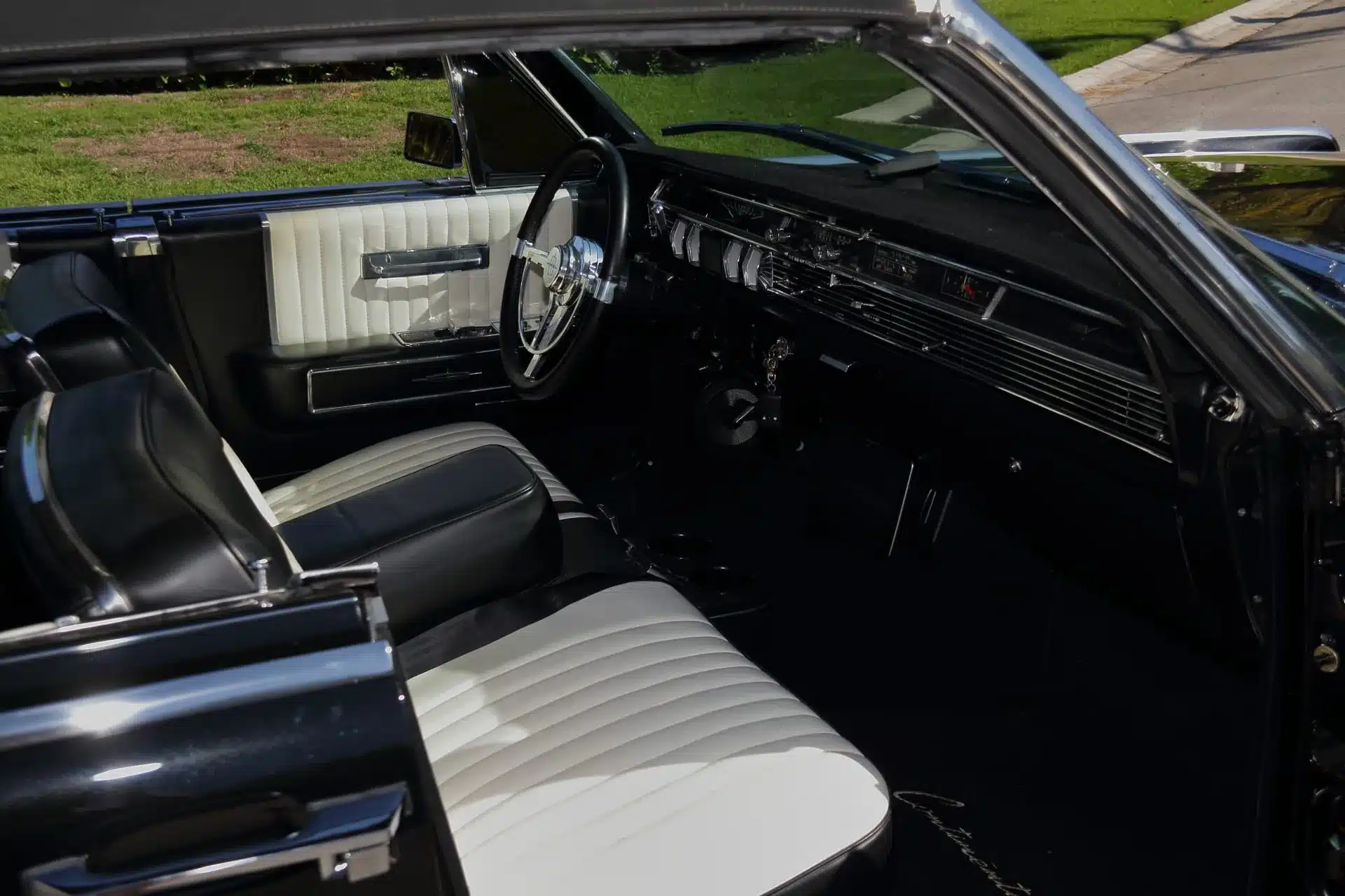 Innenraum eines 1964 Lincoln Continental Cabriolets mit geöffneter Tür, schwarz-weißen Ledersitzen und Lenkrad.