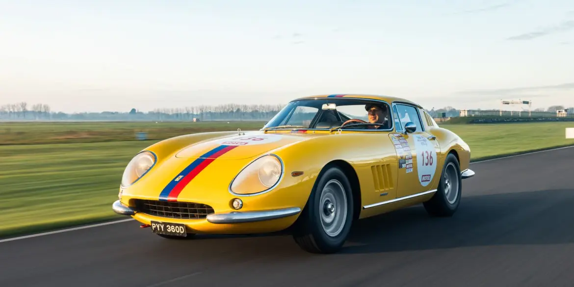 Gelber Ferrari 275 GTB Long Nose Alloy Baujahr 1965 mit blauen und roten Streifen fährt auf einer Rennstrecke.