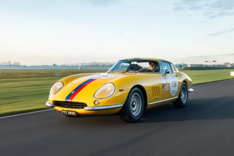 Gelber Ferrari 275 GTB Long Nose Alloy Baujahr 1965 mit blauen und roten Streifen fährt auf einer Rennstrecke.