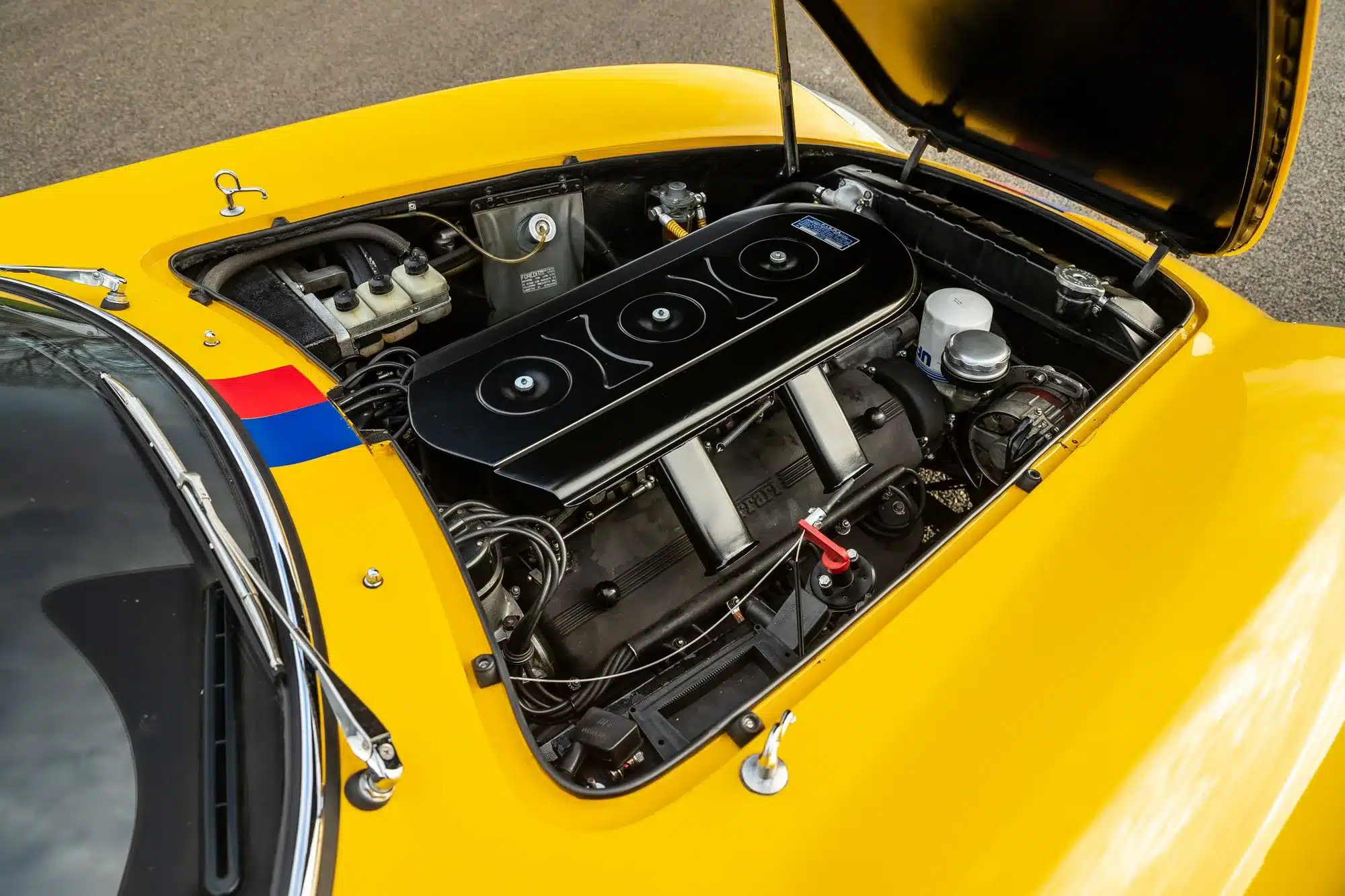 Blick in den Motorraum eines gelben Ferrari 275 GTB Long Nose Alloy mit geöffneter Motorhaube.